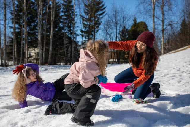 Aikuinen ja kaksi lasta pulkkamäessä.